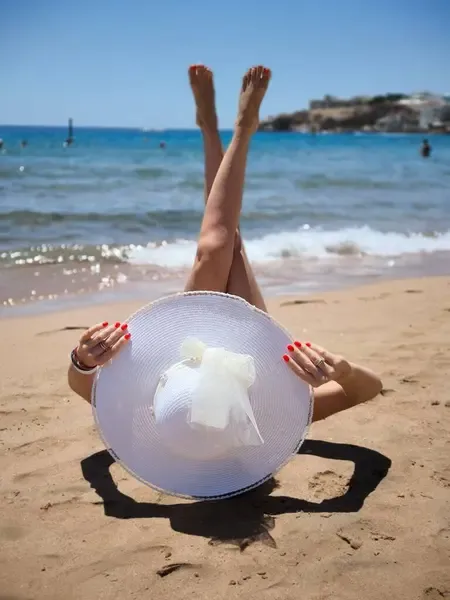 Woman on the beach hiding behind a stretched hat